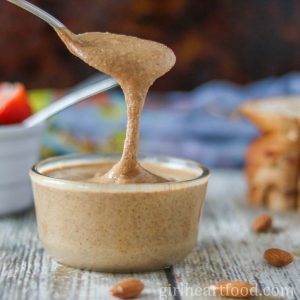 Spoonful of roasted almond butter dripping into a jar underneath it.