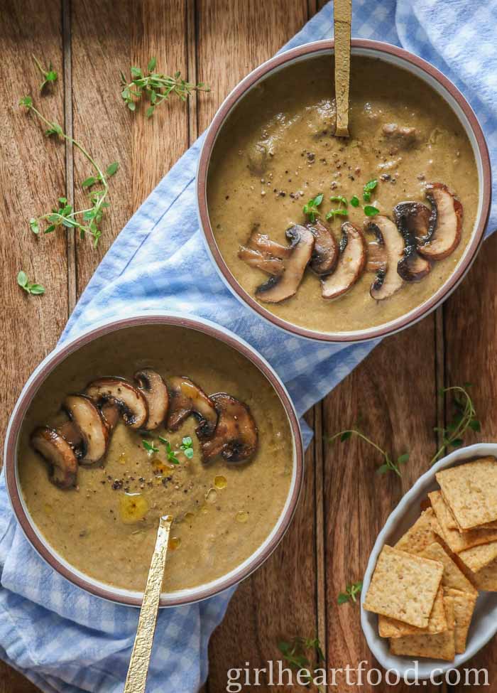 Two bowls of mushroom soup next to a dish of crackers.