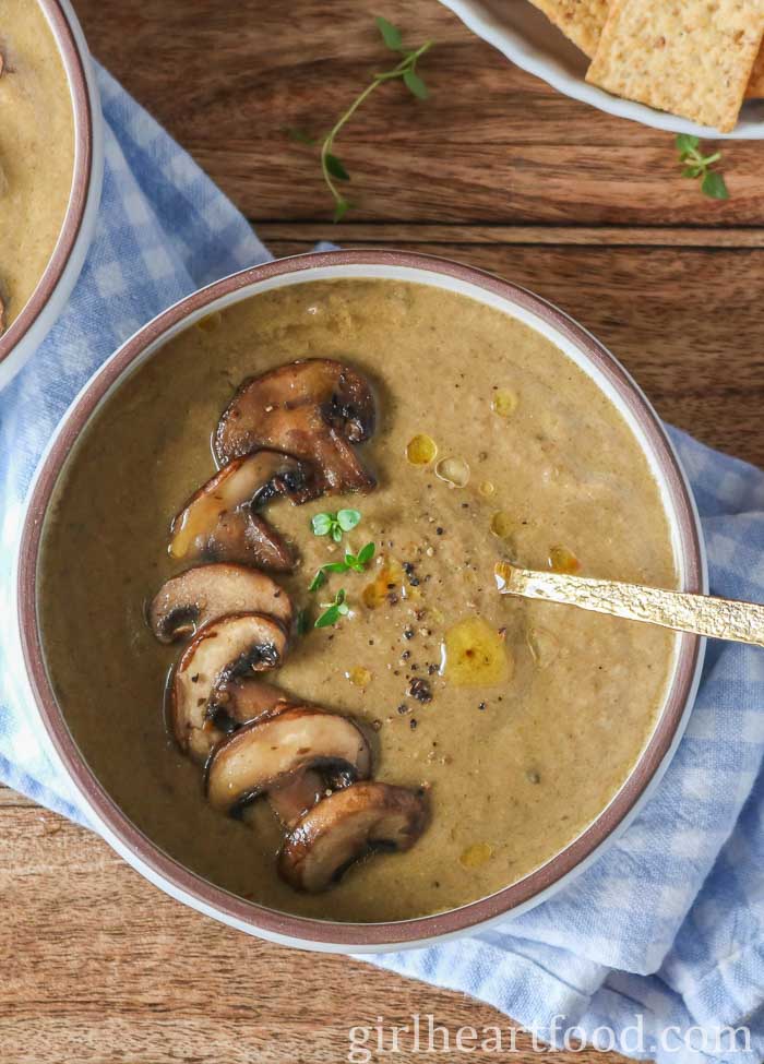 Bowl of mushroom soup garnished with mushrooms, thyme, black pepper and oil.