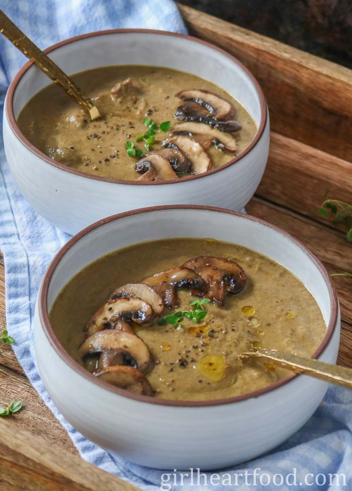 Two bowls of mushroom soup garnished with toppings, one bowl in front of the other.