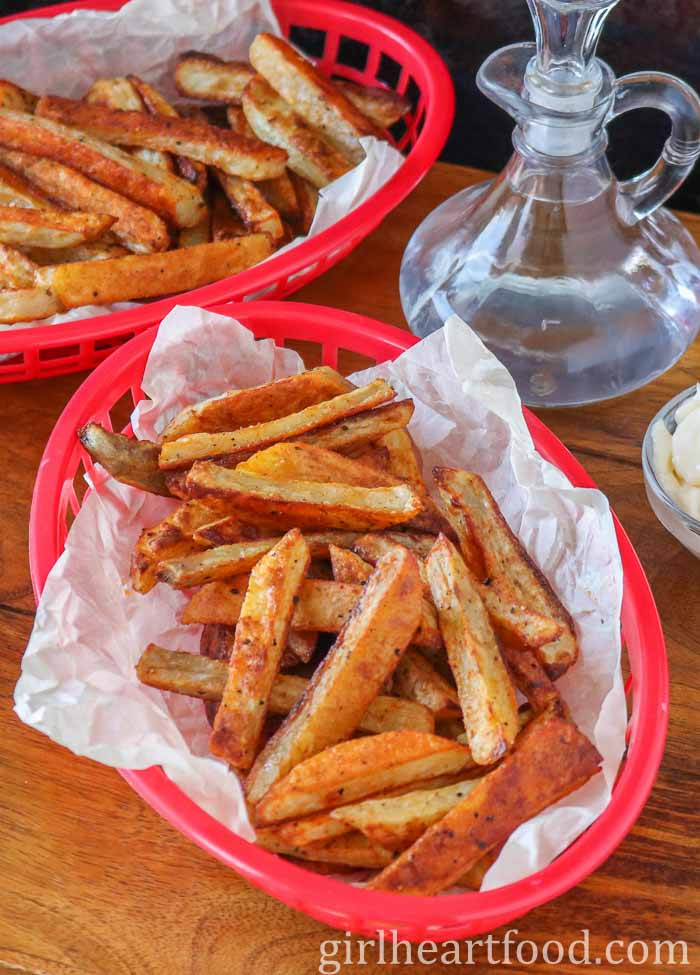 Two baskets of fries, one in front of the other, next to a bottle of vinegar.