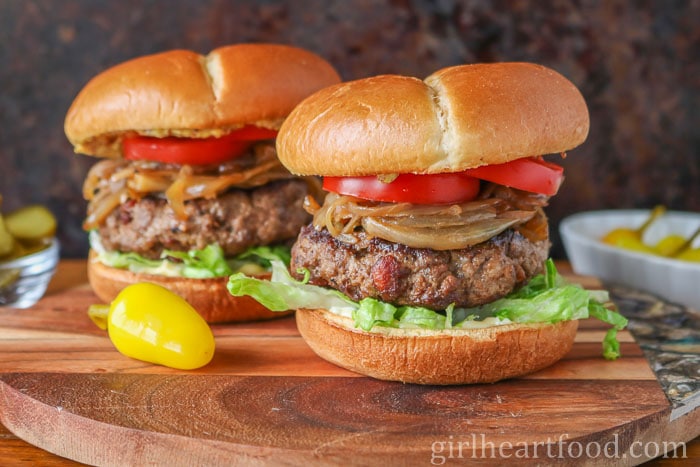 Two moose meat burgers, one in front of the other, each with toppings.