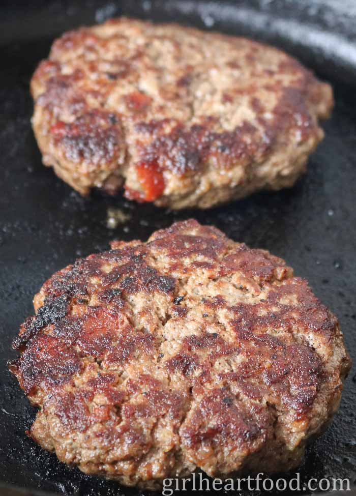 Two moose burger patties in a cast-iron skillet.
