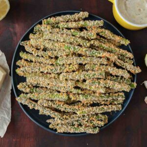 Panko parmesan crusted asparagus on a blue plate next to a dish of sauce.