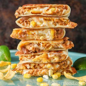 Stack of seven refried bean quesadillas with lime wedges on either side.