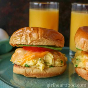 Cheesy scrambled egg sandwich with two glasses of orange juice behind it.