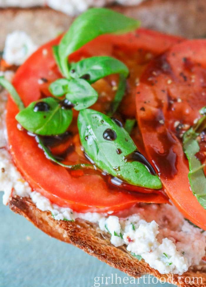 Tight close-up of ricotta cheese and tomatoes on toast with balsamic and basil.