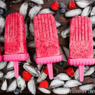 Five berry ice pops on top of a tray of ice cubes.