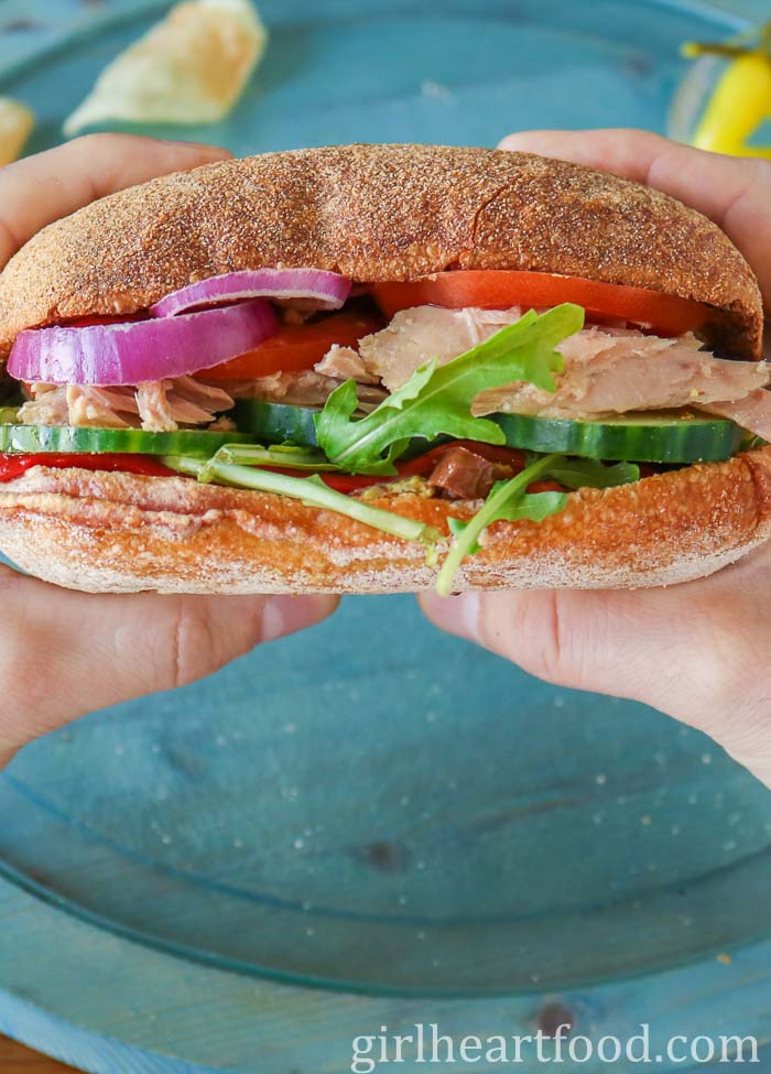 Two hands holding a tuna and vegetable sandwich on a ciabatta bun.