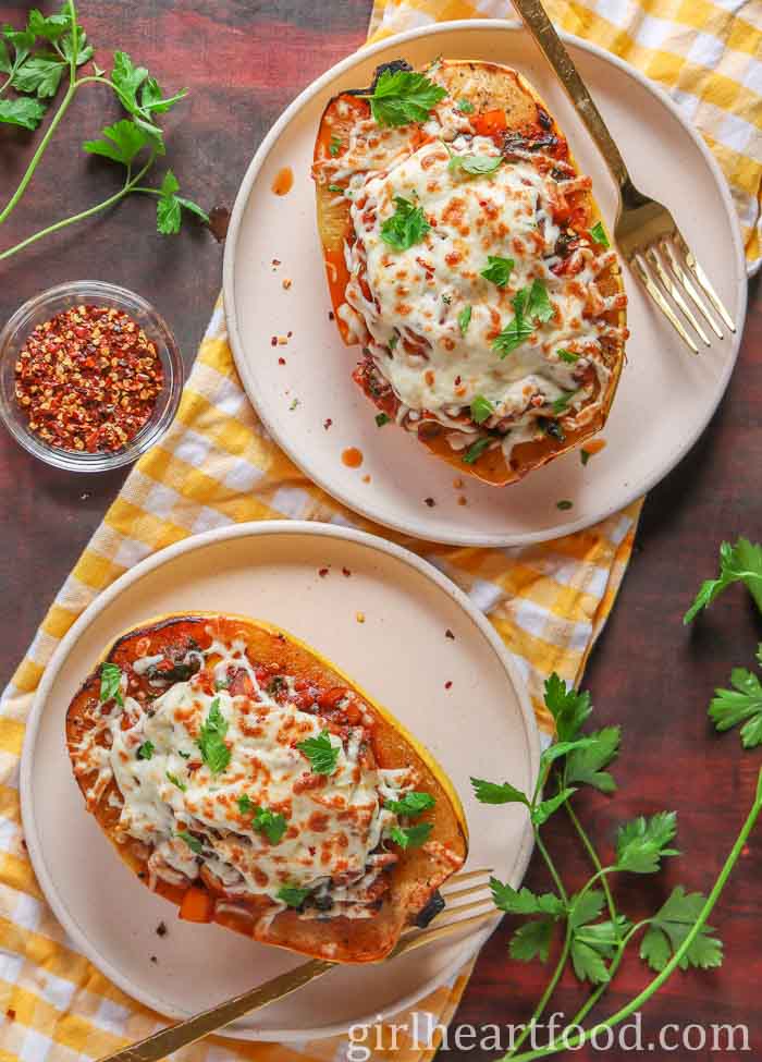 Two cheesy stuffed spaghetti squash boats, each on a plate with forks.