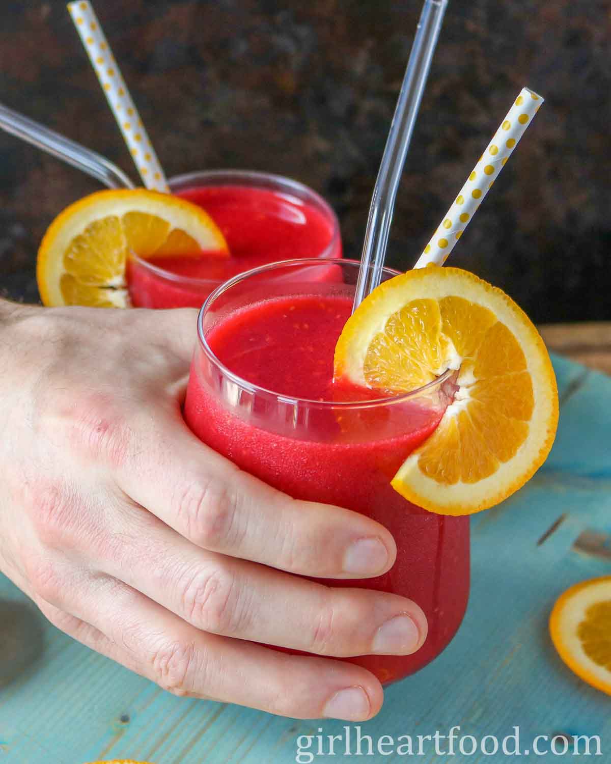 Hand holding a glass of blended frozen raspberry cocktail.