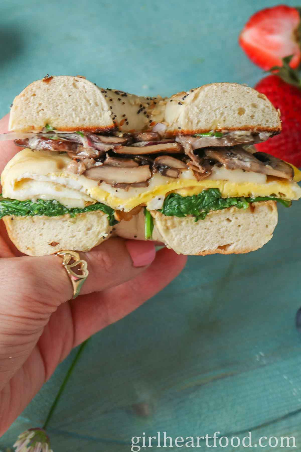 Hand holding half of a bagel breakfast sandwich.
