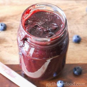 Jar of blueberry barbecue sauce alongside blueberries.
