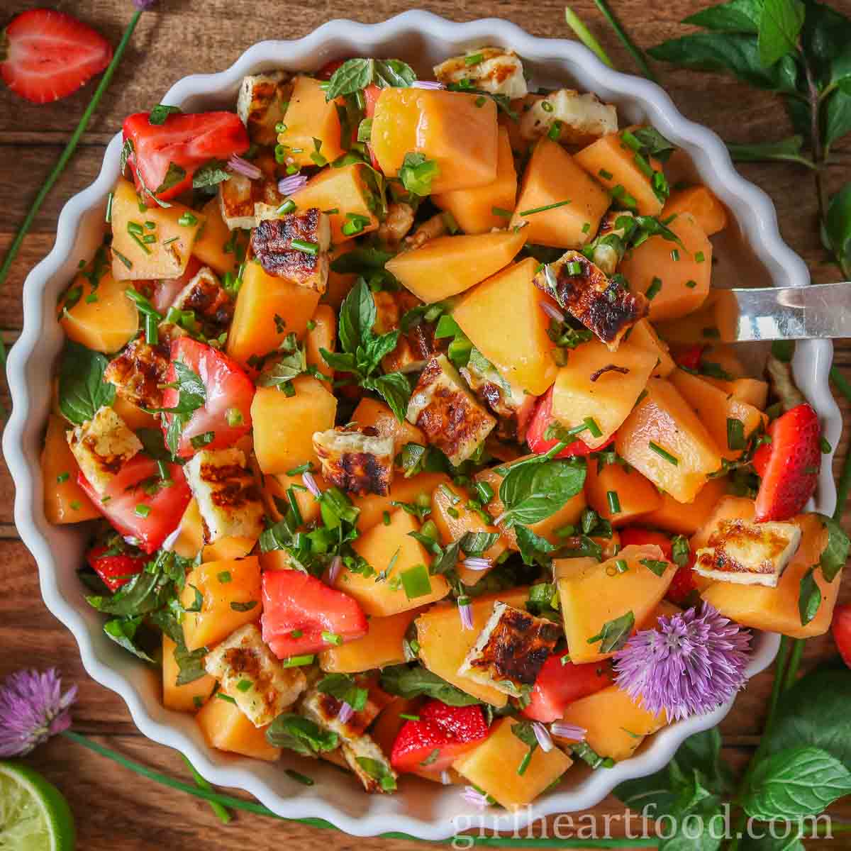 Cantaloupe salad in a bowl with a serving spoon dunked into it.