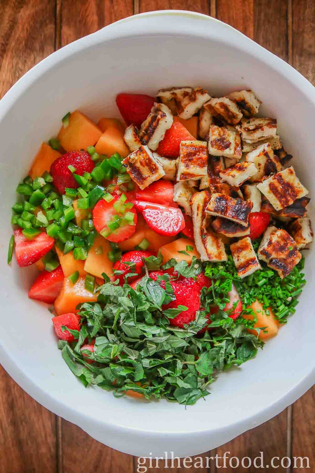 Ingredients for cantaloupe salad in a bowl, not yet mixed together.