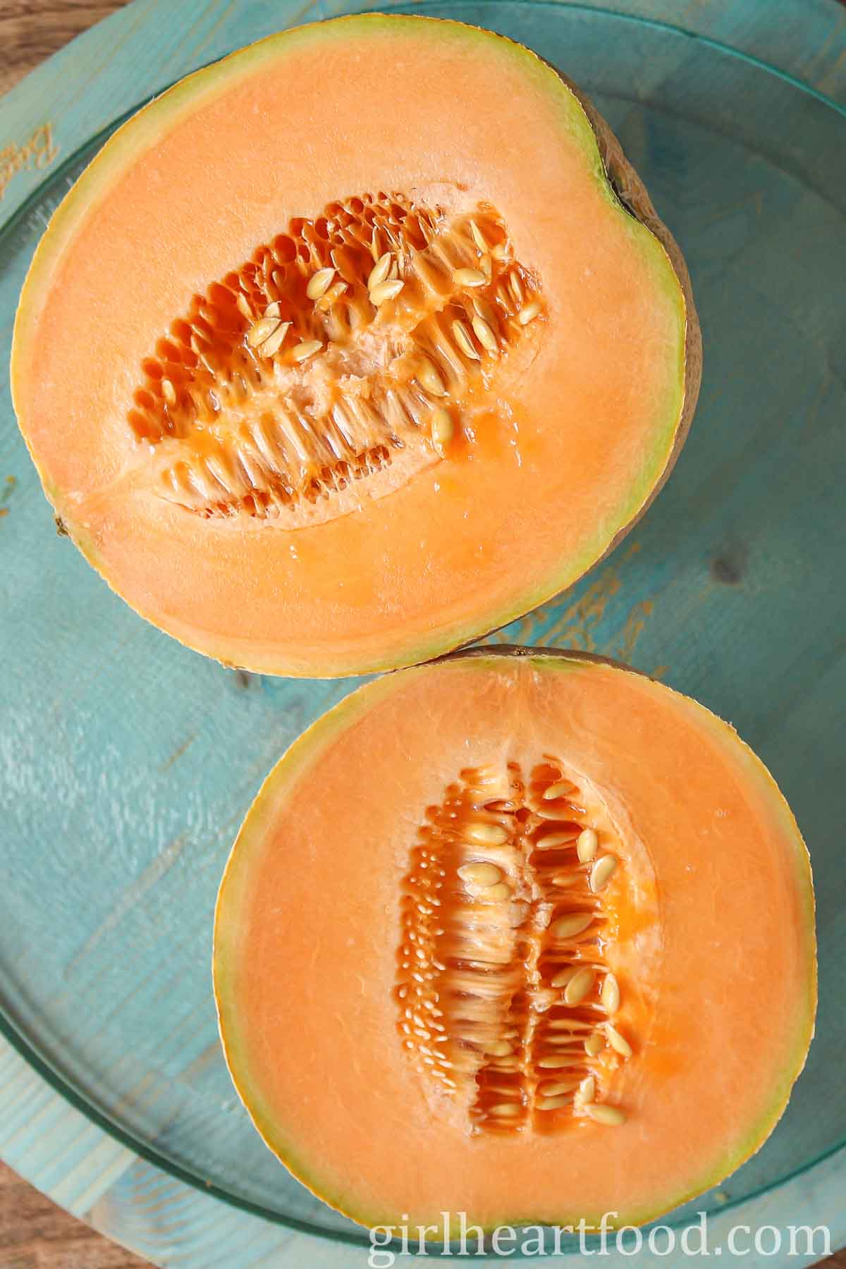 Two halves of a cut cantaloupe on a blue board.