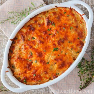 Cheesy scalloped potatoes in a casserole dish garnished with thyme.