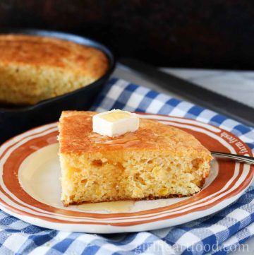 Slice of cornbread on a plate with a dab of butter and honey over top.