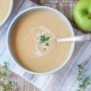 Bowl of creamy parsnip apple soup next to a green apple.