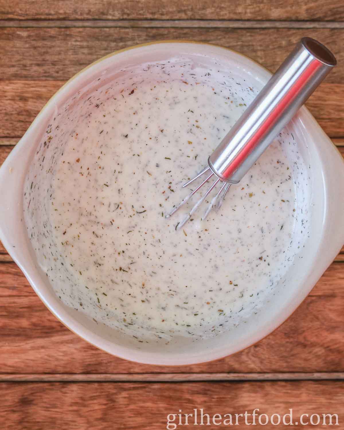 Bowl of creamy yogurt dressing with a small whisk dunked into it.