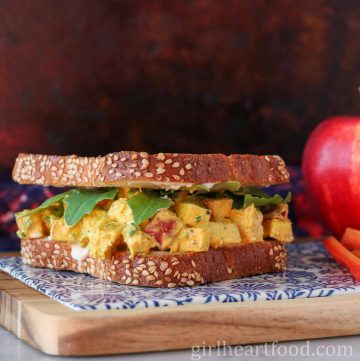Curry chicken salad sandwich with apple next to an apple and carrot sticks.