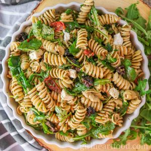 Bowl of Mediterranean pesto pasta salad next to a tea towel and arugula.