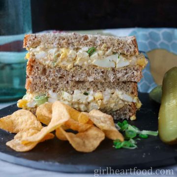 Stack of two halves of a classic egg salad sandwich next to potato chips.