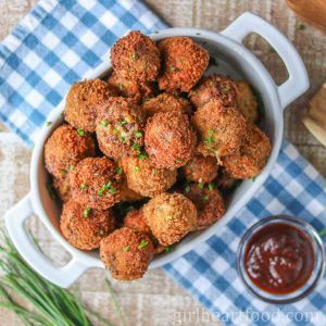 Fried mashed potato balls in a dish next to BBQ sauce and chives.