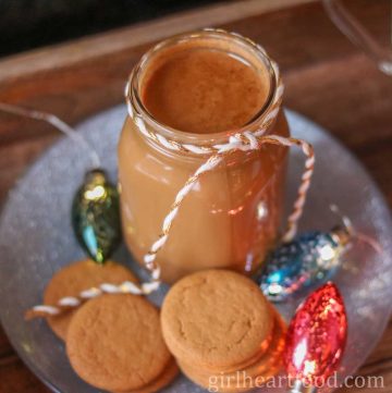 Jar of gingerbread coffee creamer, cookies and holiday lights on a silver plate.