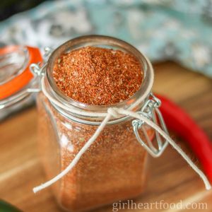 Glass jar of homemade taco seasoning next to a red chili pepper.