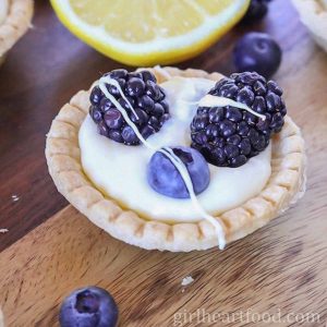 Mini lemon cream tart with fresh berries and white chocolate drizzle.