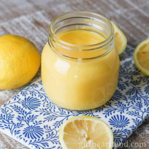 Jar of homemade lemon curd next to lemon halves.