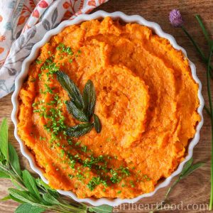 Dish of mashed butternut squash and sweet potato garnished with chives and sage leaves.