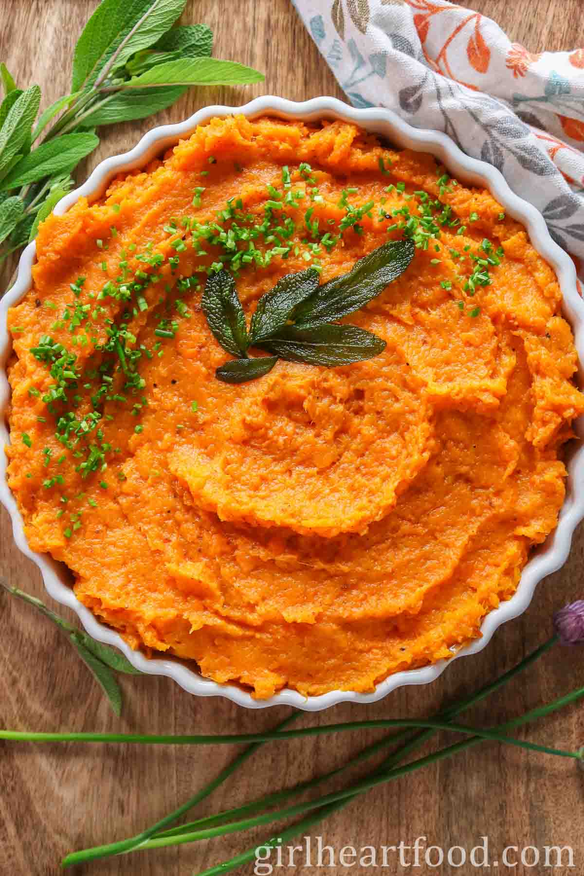 Dish of mashed butternut squash and sweet potato garnished with chives and  sage leaves.