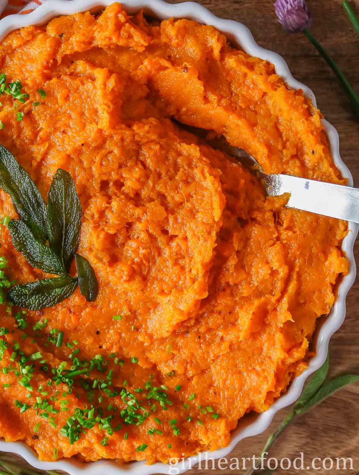 Dish of butternut squash sweet potato mash with a serving spoon dunked into it.