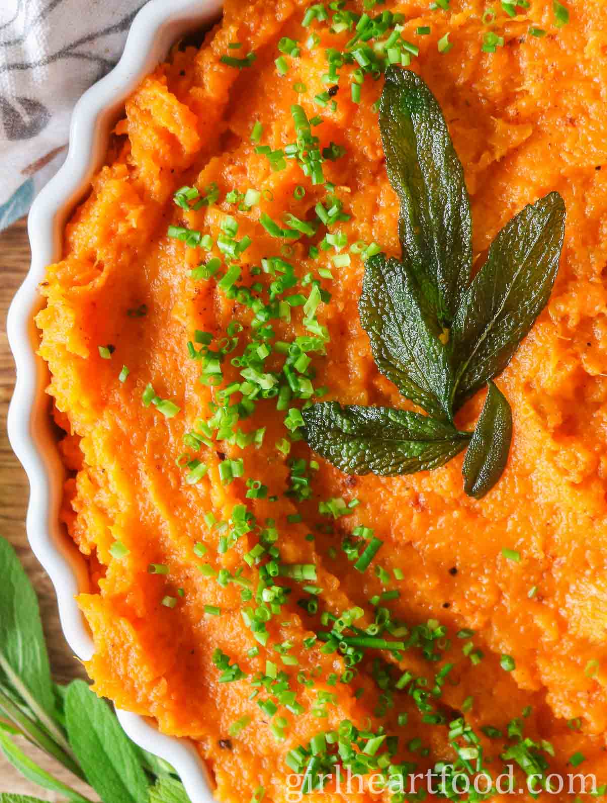 Close-up of mashed butternut squash & sweet potato garnished with chives & sage leaves.