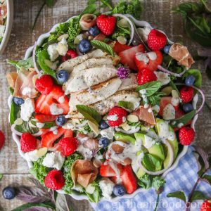 Bowl of green salad with poppy seed dressing drizzled over top.