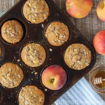 Peach muffins in a muffin pan alongside fresh peaches and dish of honey.