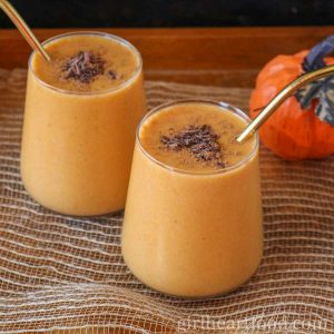 Two glasses of pumpkin smoothie topped with chocolate, sitting next to an ornamental pumpkin.