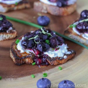 Roasted blueberry and goat cheese crostini next to blueberries and chives.