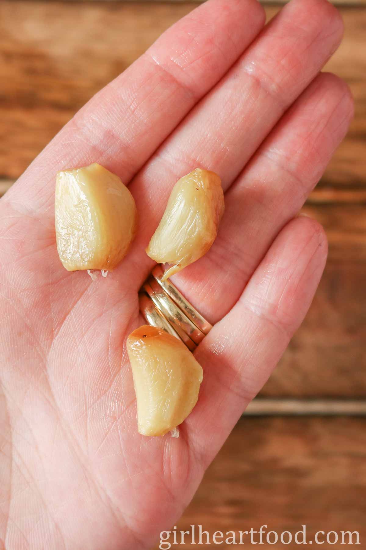Hand holding three cloves of roasted garlic.