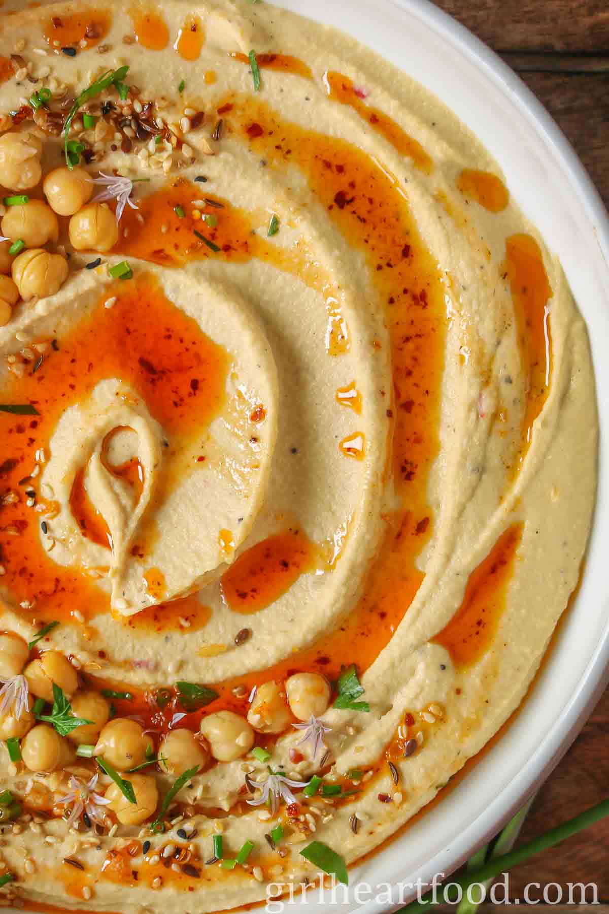 Close-up of a bowl of roasted garlic hummus garnished with toppings.