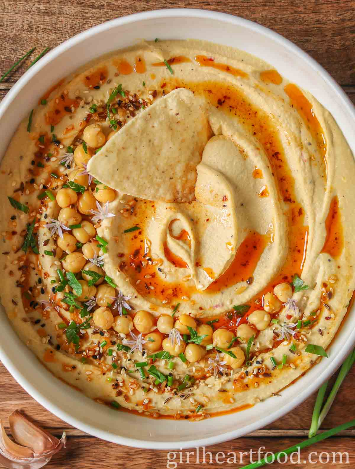 Bowl of creamy hummus with a tortilla chip dunked into it.