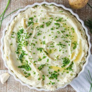 Dish of garlic mashed potatoes garnished with chives and melted butter.