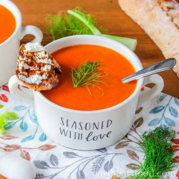 Bowl of roasted red pepper tomato fennel soup with a crostino resting on the bowl.