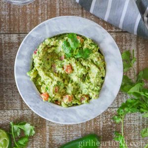 Bowl of guacamole next to cilantro, jalapeno and a tea towel.