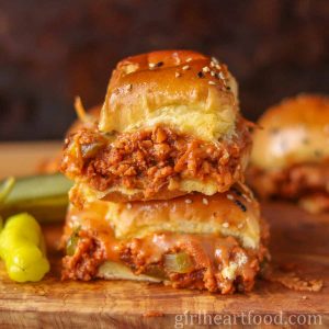 Stack of two cheesy vegetarian sloppy joe sliders next to a hot pepper.