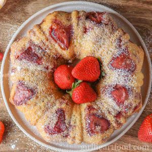Strawberry cake on a plate dusted with icing sugar and fresh strawberries in the centre.