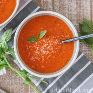 Bowl of tomato soup next to basil.