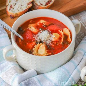 Bowl of tomato tortellini soup garnished with Parmesan cheese.